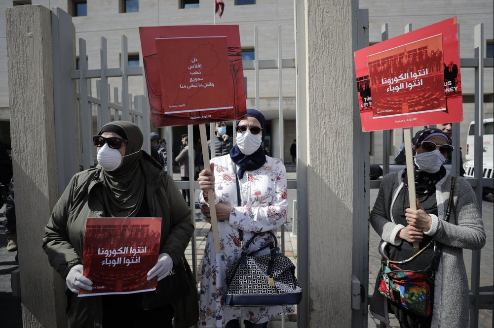 Anti-government protesters hold up banners in Arabic that read, 'You are the coronavirus, you are the epidemic,' and 'Humiliation, bankruptcy, looting, starving and killing the rest of us,' in front of the Lebanese Ministry of Health, in Beirut, Lebanon 