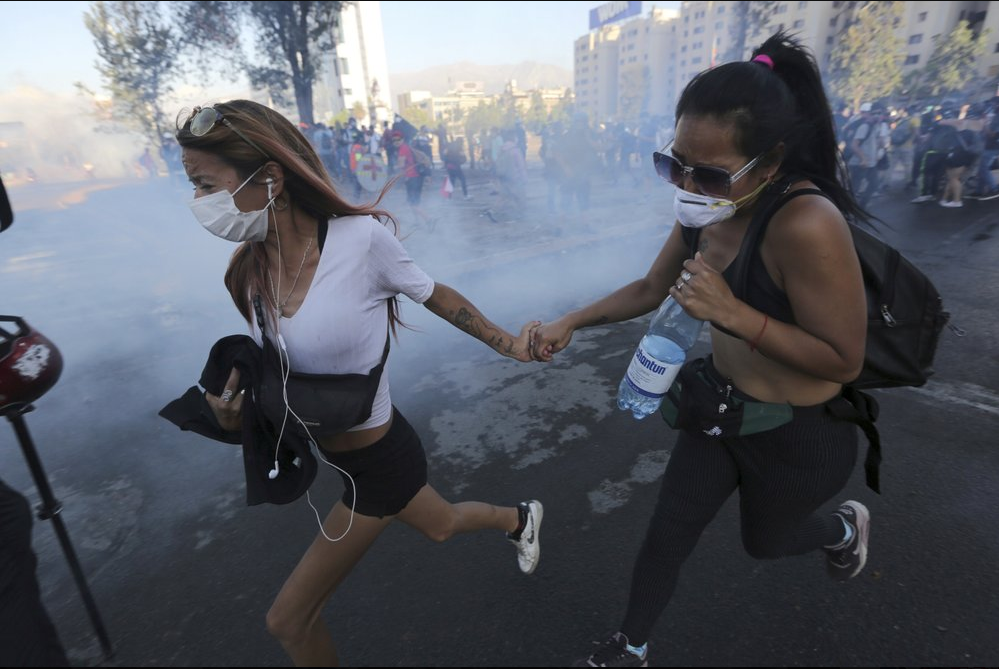 Anti-government demonstrators run from a cloud of teargas during clashes with police in Santiago, Chile 