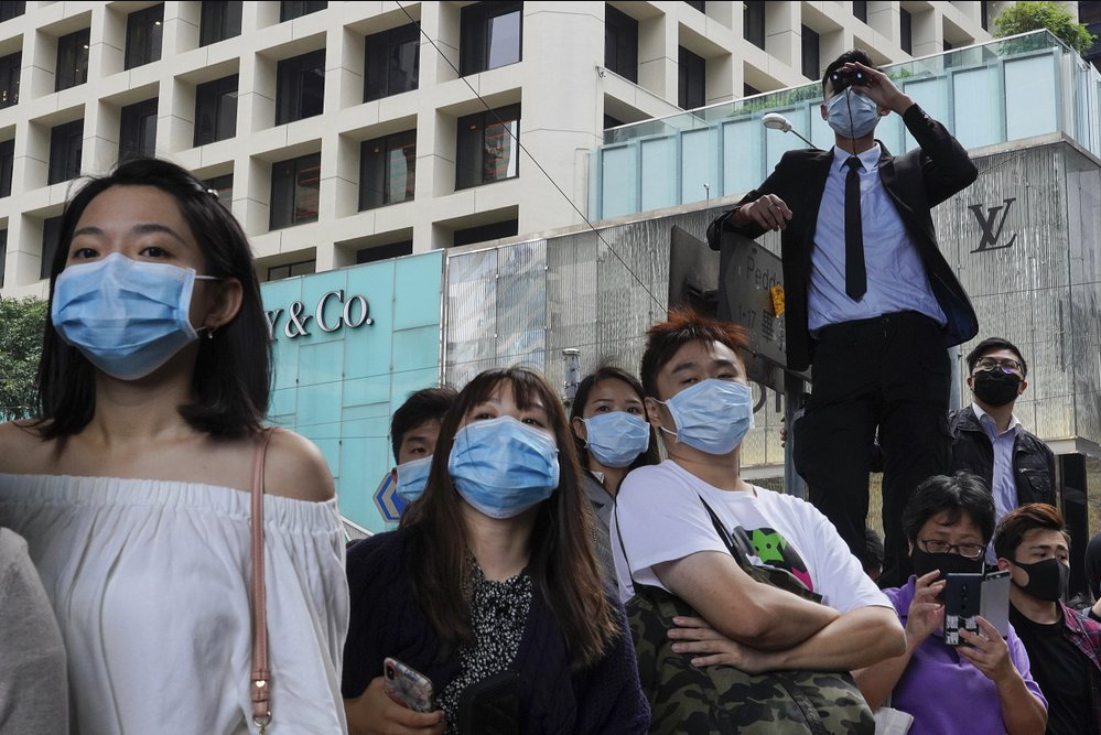People wearing face masks watch pro-democracy protesters in Hong Kong 