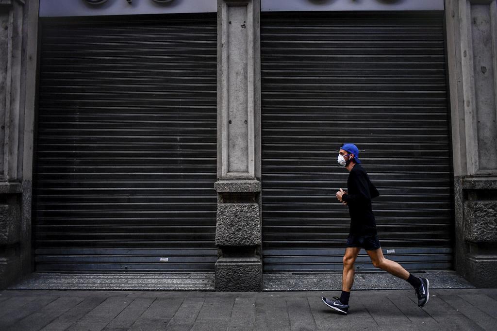 A jogger wearing a face mask runs past a shuttered business in Milan 