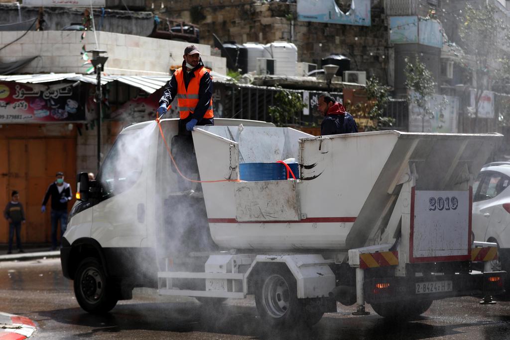 Palestinian municipality employees spray disinfectant in the West Bank town of Hebron, 24 March 2020 