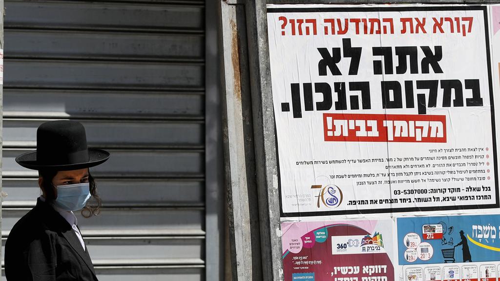 A Bnei Brak resident stands next to a poster urging residents to stay home. 'Reading this notice? You are in the wrong place,' the poster says 