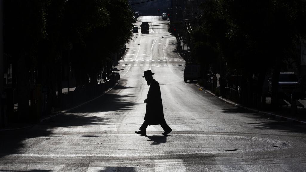 An ultra-Orthodox Jew crosses a mainly deserted street because of the government's measures to help stop the spread of the coronavirus, in Bnei Brak 