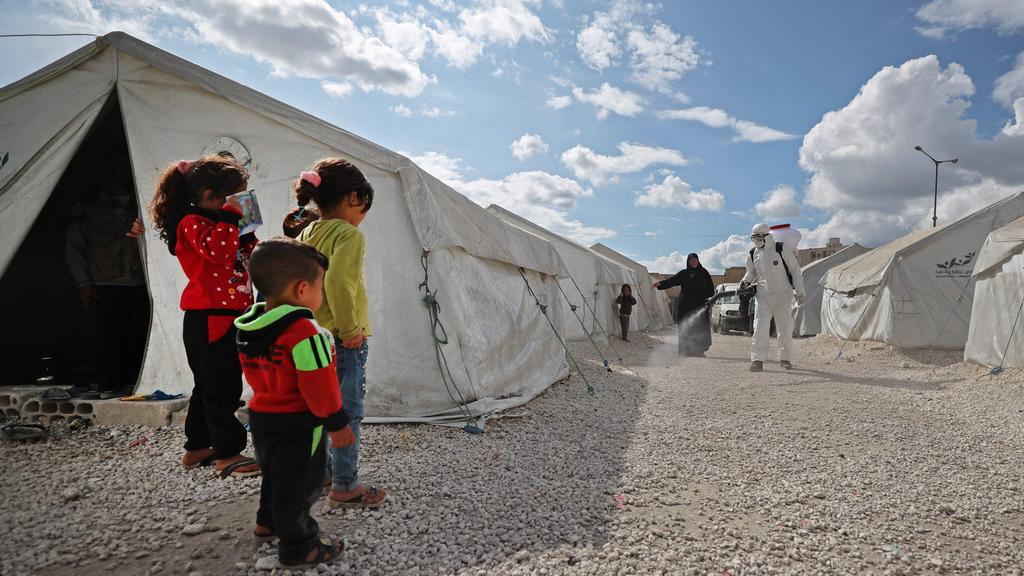 Displaced Syrian children watch as a sanitation worker disinfects their camp next to the Idlib municipal stadium 