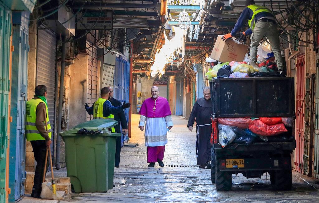 Archbishop Pierbattista Pizzaballa walks past garbage collectors in the Old City of Jerusalem as he makes his way to the Church of the Holy Sepulchre for the Easter Sunday service, April 12, 2020 
