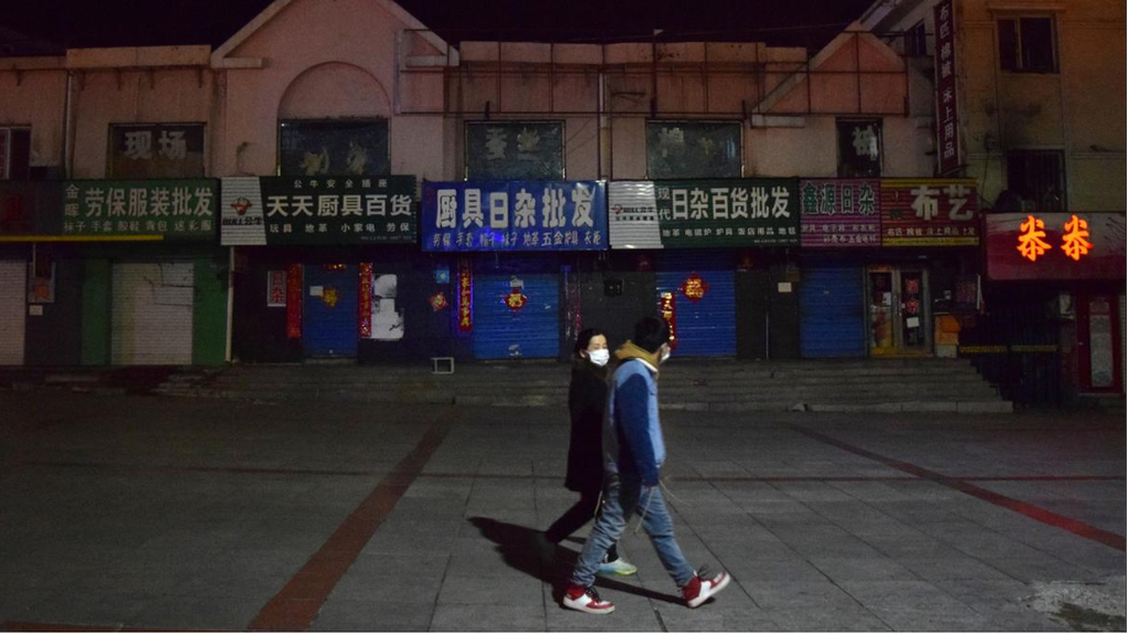 People wearing face masks walk past closed shops in the city centre of Suifenhe, China 