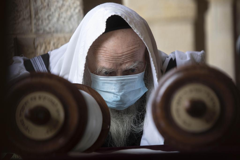 A man wears a face mask to curb the spread of the coronavirus as he reads from a Torah scroll at the Western Wall, the holiest site where Jews can pray in Jerusalem's old city 
