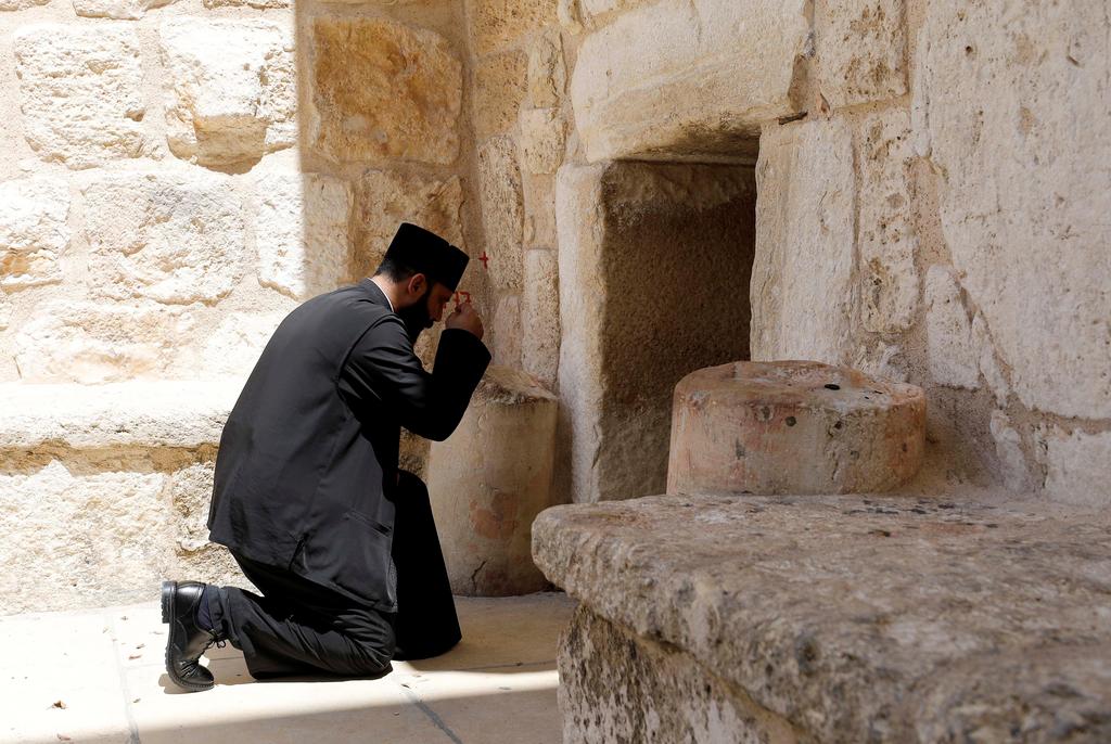 A priest kneels outside the Church of the Nativity closed due to COVID-19