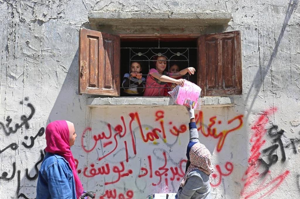Eilya Alzra’ei (right) and Riham Basheer distributing storybooks, paper, and crayons, Deir Albalah camp