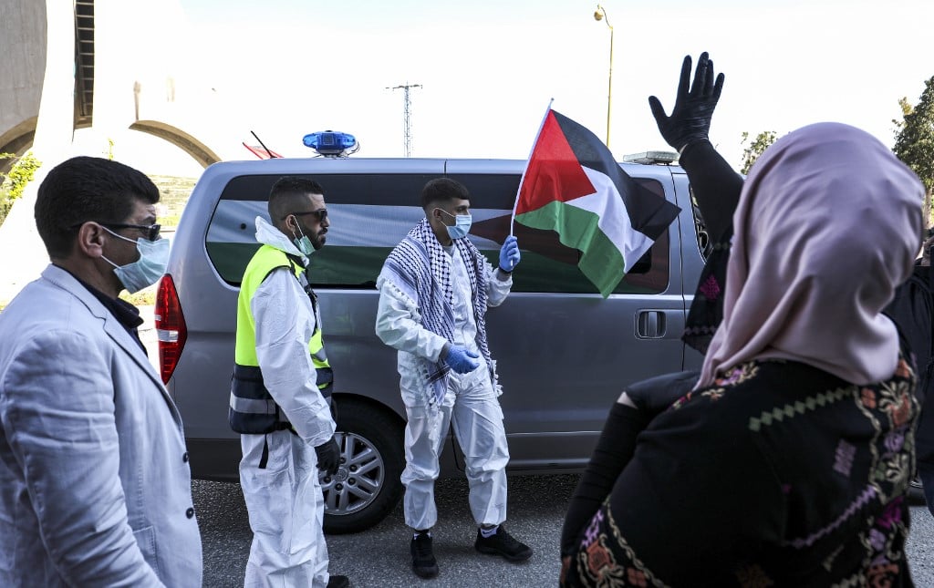 Amir Naji, an 18-year-old Palestinian released by Israel from prison, waves a Palestinian flag while clad in a surgical mask and latex gloves due to the coronavirus pandemic as he is received by his family at a checkpoint near the city of Ramallah in the West Bank 