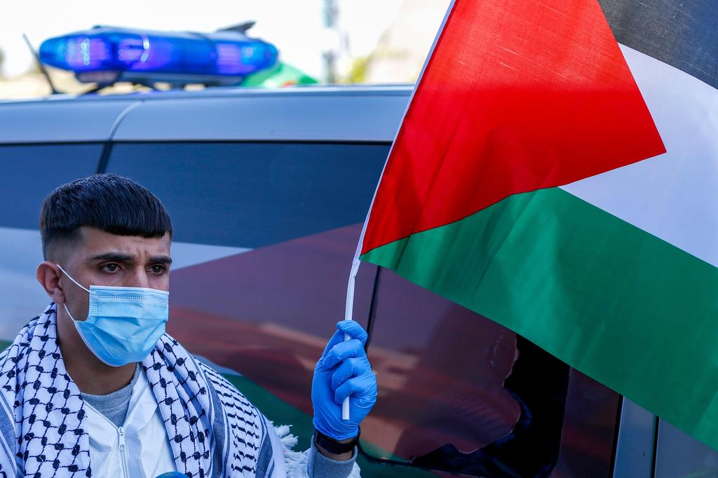Amir Naji, an 18-year-old Palestinian released by Israel from prison, waves a Palestinian flag while clad in a surgical mask and latex gloves due to the COVID-19 coronavirus pandemic as he arrives to be received by his family at a checkpoint near the city of Ramallah 