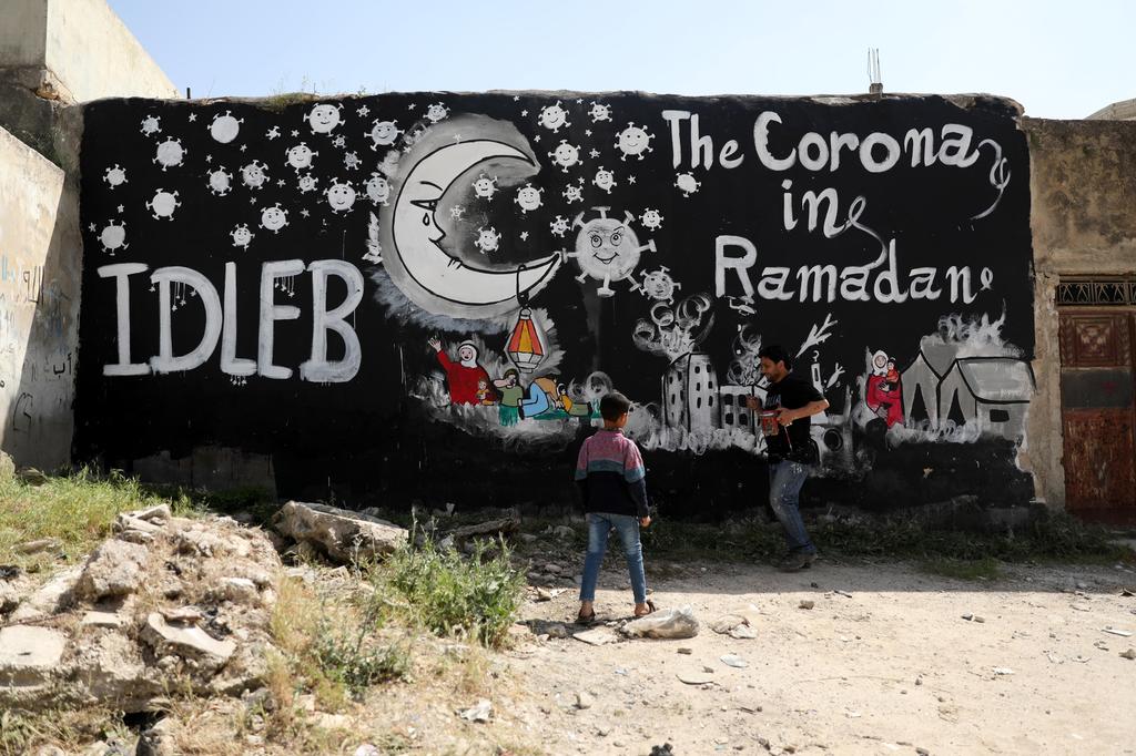 Syrian people stand near a graffiti painted due to the ongoing pandemic of the Covid-19 disease, in Idlib, Syria