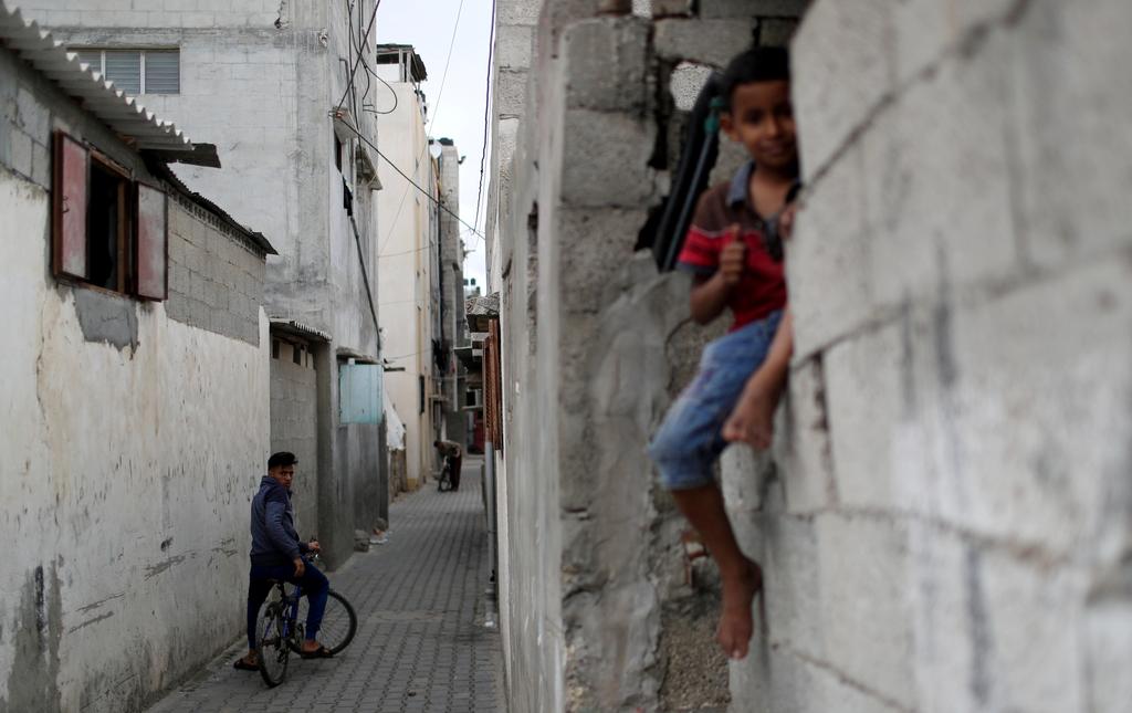 A Palestinian youth on a bicycle looks on as a boy sits on a wall in Jabalia refugee camp 
