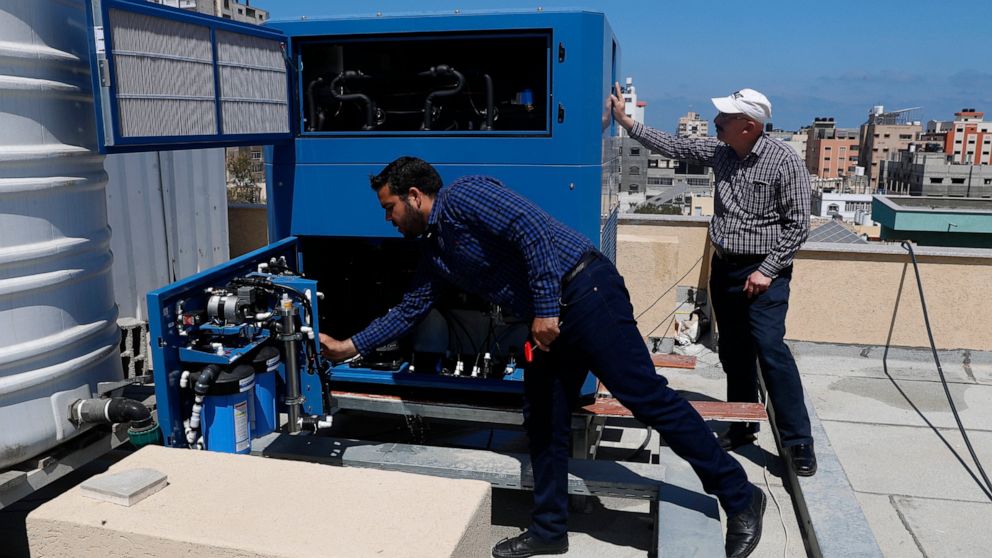 Palestinian engineer Raed Nakhal from Palestine Children Relief Fund, right, and engineer Abdullah Dewik, check the GEN-M machine that generates safe drinking water from air at the roof of al-Rantisi pediatric hospital in Gaza City 