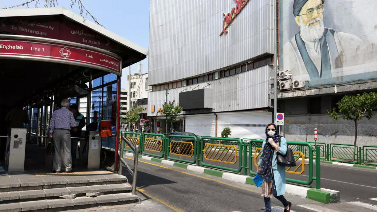 A woman wearing a protective face mask outside the entrance to a metro station in Tehran 