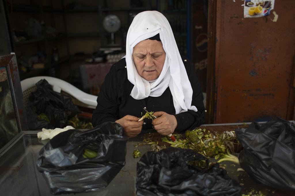 A woman cleans zucchini and wild artichokes for customers outside her empty mini-market in Bab al-Tebanneh, one of Tripoli's poorest slums  