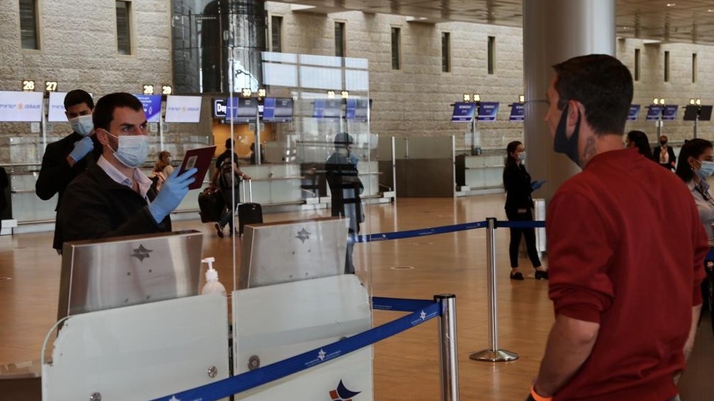 A masked official examines the passport of a traveler at a near-deserted Ben-Gurion Airport during the pandemic 