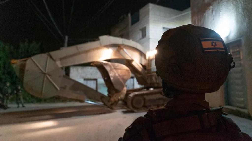An IDF soldier watches a bulldozer about to demolish the home of Omar Amin Abu Laila in the Zawiya neighborhood of Nablus at dawn, April 24, 2019