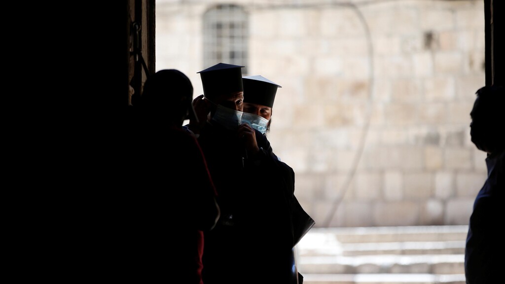 Members of the clergy wear masks as they stand near the entrance of Church of the Holy Sepulchre in Jerusalem 