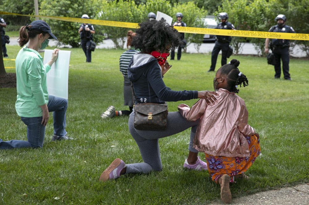 Ericka Ward-Audena, of Washington, puts her hand on her daughter Elle Ward-Audena, 7, as they take a knee in front of a police line during a protest of President Donald Trump's visit to the Saint John Paul II National Shrine 