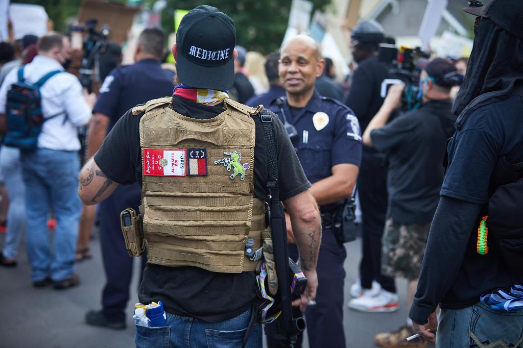 A member of the far-right militia, Boogaloo Bois, walks next to protestors demonstrating outside Charlotte Mecklenburg Police Department Metro Division 2 just outside of downtown Charlotte, North Carolina 