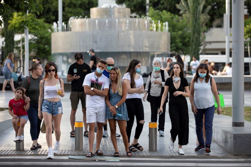 Pedestrians, some wearing masks, prepare to cross the street at Dizengoff Square 
