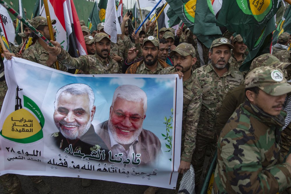 Iraqi militiamen march and chant anti U.S. slogans while carrying a picture of Soleimani, left and al-Muhandis, with Arabic that reads 'our martyr leaders' 