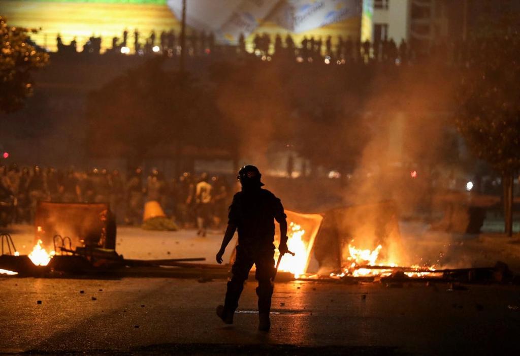 A member of the Lebanese riot police walks near burning fire during a protest against the fall in pound currency and mounting economic hardship, in Beirut, Lebanon 