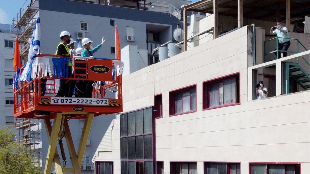 Israelis in protective masks greet loved ones on the roof of a retirement home using an elevated platform made available by Netanya municipality
