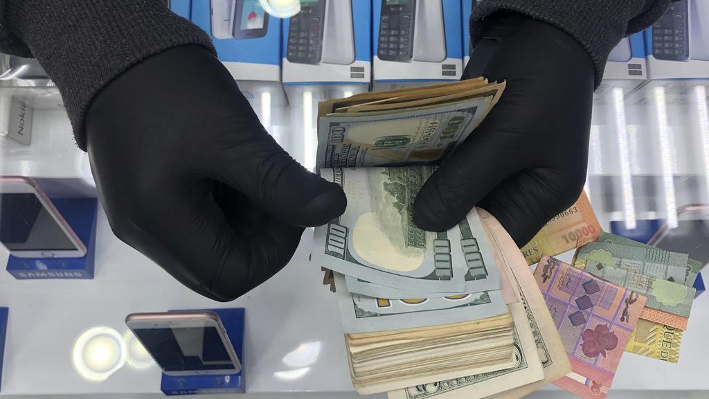 , a cell phone shop owner wears gloves as he counts U.S. dollars, in Beirut, Lebanon