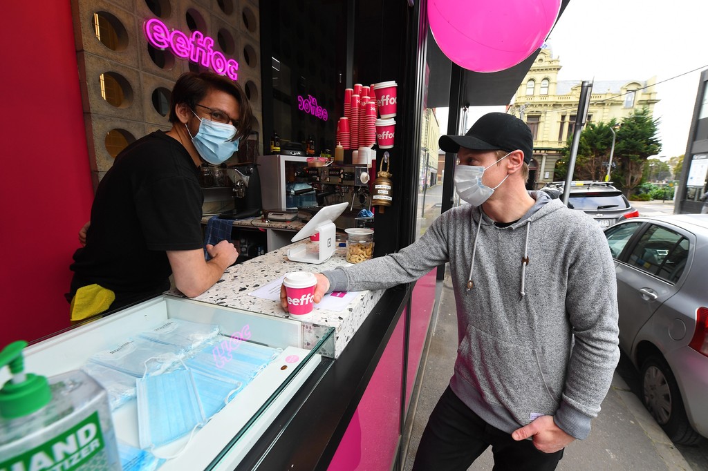 Barista Alex Pallas (L) serves a customer a coffee and a face mask at Eeffoc Cafe in Prahran, Melbourne, Australia 