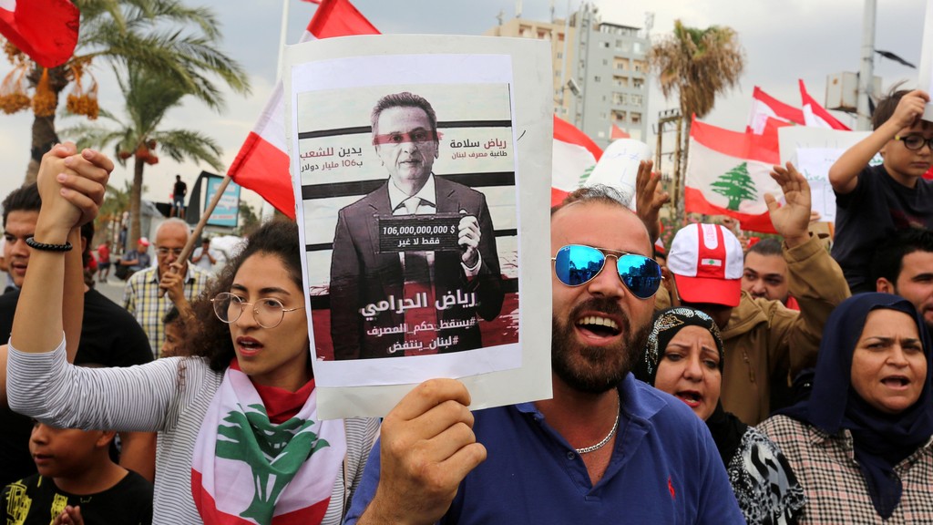  Demonstrators carry Lebanese flags and a banner depicting Lebanon's Central Bank Governor Riad Salameh, as they head towards the central bank building during an anti-government protest