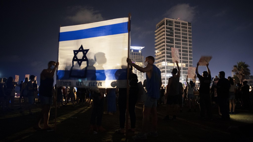 Protesters hold the Israeli national flag during a protest against Israel's Prime Minister Benjamin Netanyahu in Tel Aviv