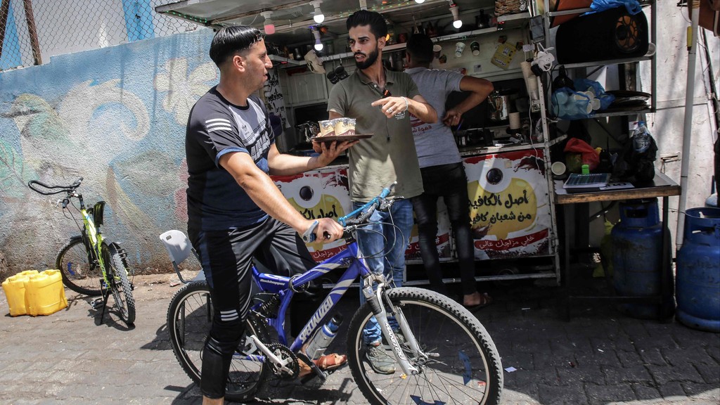 Hamuda gives instructions to one of his delivery employees carrying a tray of steaming cups of coffee, in front of his small stand near Rafah