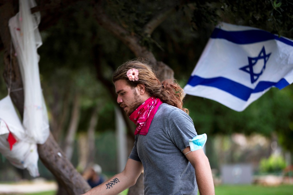 A young man walks past an Israeli flag at a protest camp site near the prime minister's Jerusalem residence 