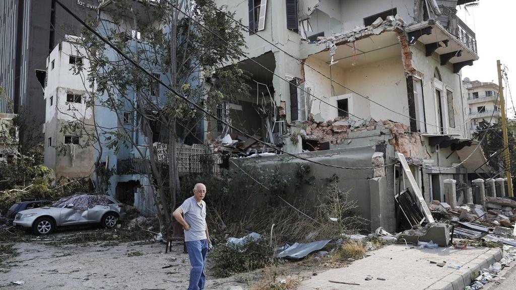 A Lebanese man stands next to his damaged house near the scene where an explosion hit on Tuesday the seaport of Beirut, Lebanon 