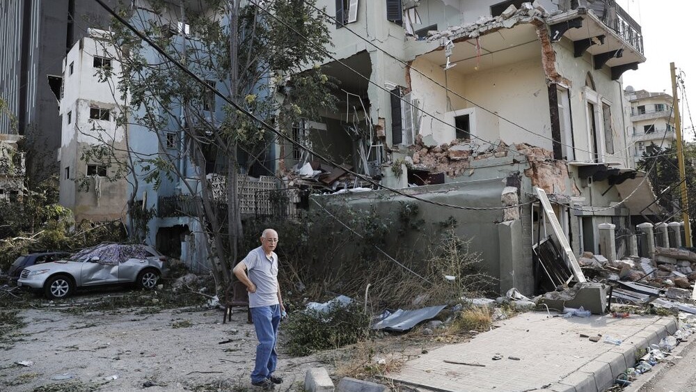 A Lebanese man stands next to his damaged house near the scene where an explosion hit on Tuesday the seaport of Beirut, Lebanon 