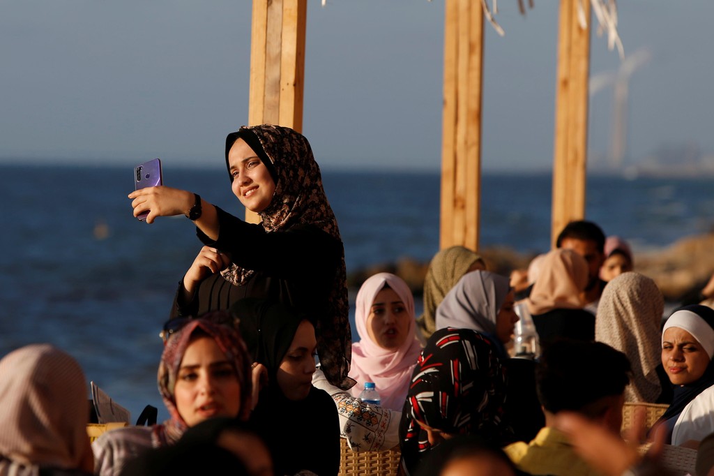 A Palestinian woman takes a selfie as families sit at "Maldive Gaza" cafe on a beach in Gaza City 