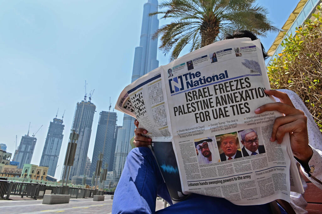 A man sits near the Burj Khalifa tower in Dubai as he reads about Israel-UAE deal
