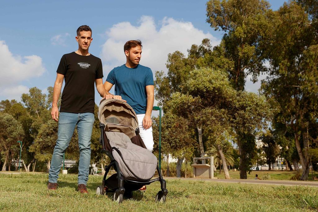 Harel Barak (L) and his husband Yakir Kanneli (R) pose for a picture with an empty stroller at a park in the Israeli coastal city of Tel Aviv 