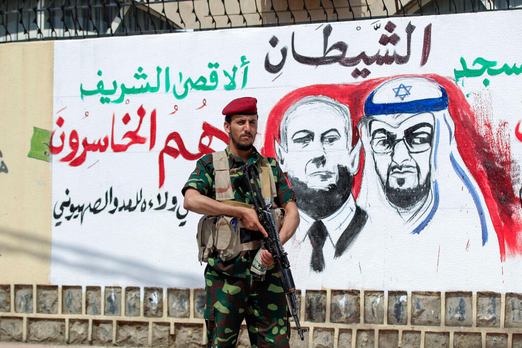 A fighter loyal to Yemen's Huthi rebels stands guard next to a mural denouncing Abu Dhabi Crown Prince Sheikh Mohammed bin Zayed Al Nahyan (R) and Israeli Prime Minister Benjamin Netanyahu