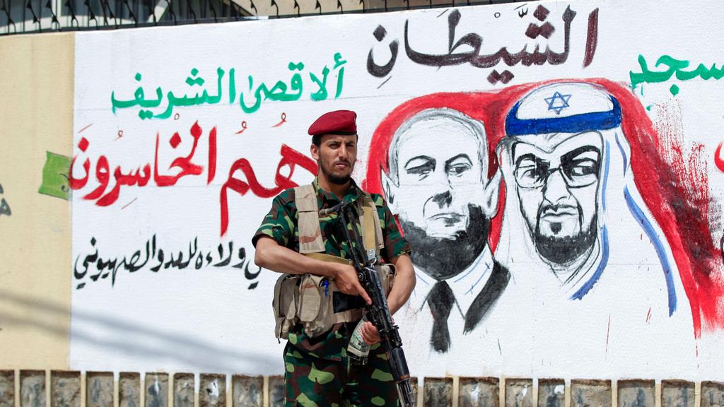 A fighter loyal to Yemen's Huthi rebels stands guard next to a mural denouncing Abu Dhabi Crown Prince Sheikh Mohammed bin Zayed Al Nahyan (R) and Israeli Prime Minister Benjamin Netanyahu