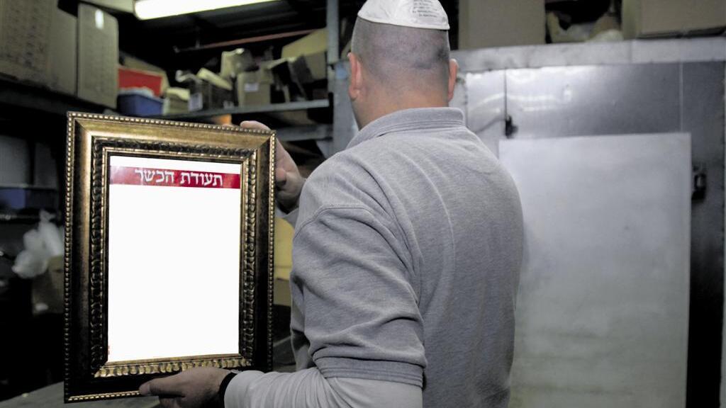 An Israeli business owner holding his kashrut certificate (Photo: Gil Lerner) An Israeli business owner holding his kashrut certificate
