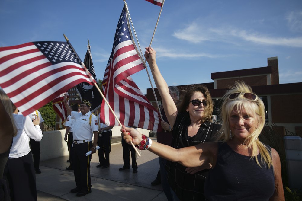 Melissa Moore, right, a Republican who is running for a seat in the Minnesota Legislature, waves an American flag with members of VFW 7051 in the background in St. Louis Park, Minn. 