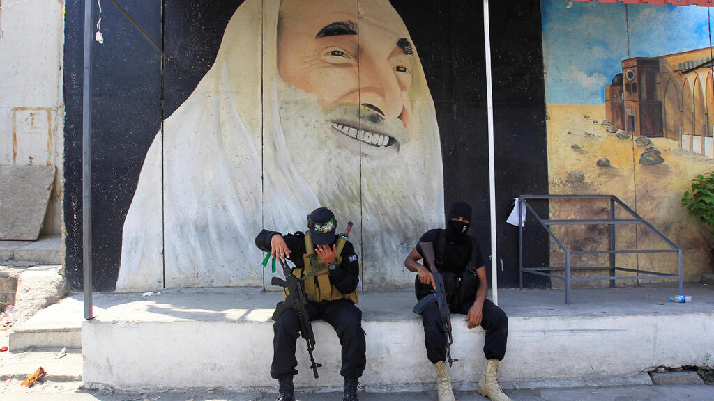 Militants from the Palestinian group Hamas, sit in front of a mural depicting late Hamas leader Ahmed Yassin, as the group's top leader, Ismail Haniyeh, visits at Ain el Hilweh Palestinian refugee camp in Sidon, Lebanon 