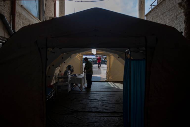 A Palestinian medic checks a person's temperature to screen for coronavirus symptoms, inside a temporary tent at the entrance al-Quds Hospital, in Gaza City 