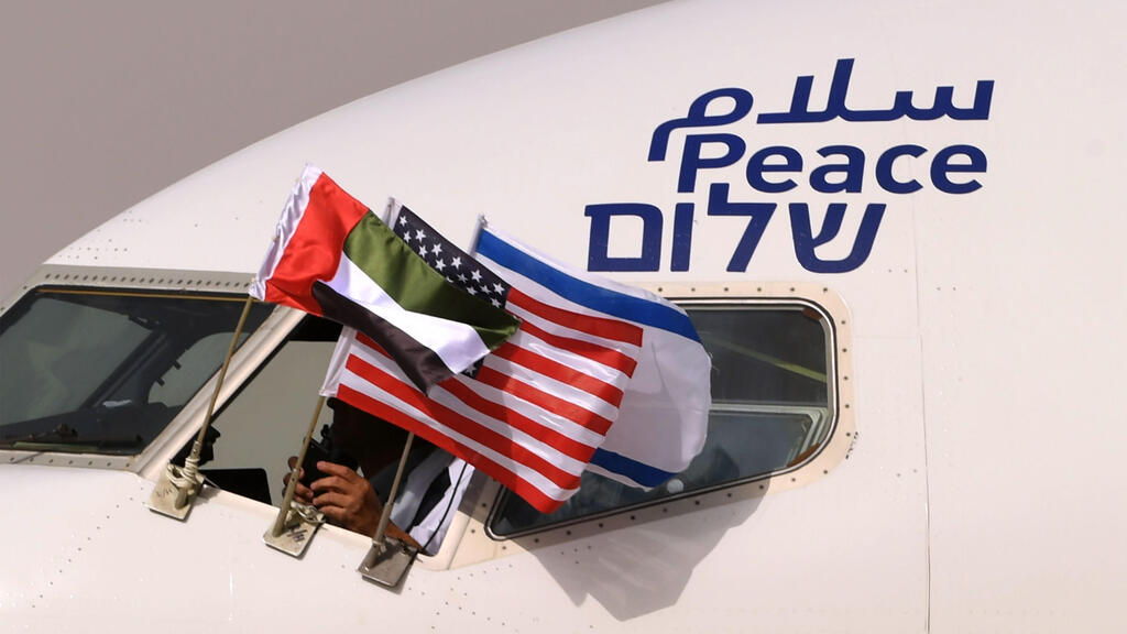the Emirati, Israeli and US flags are picture attached to an air-plane of Israel's El Al, adorned with the word "peace" in Arabic, English and Hebrew