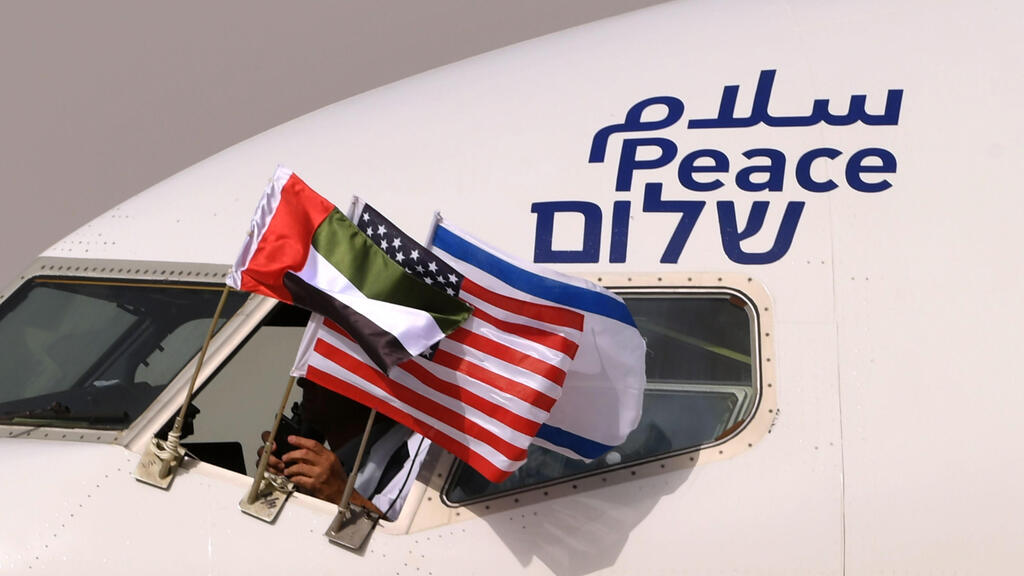 the Emirati, Israeli and US flags are picture attached to an air-plane of Israel's El Al, adorned with the word "peace" in Arabic, English and Hebrew