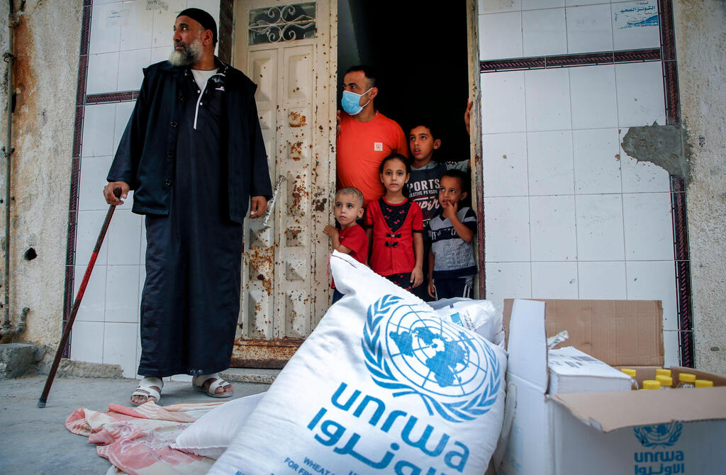 Members of a Palestinian family, some clad in mask due to the COVID-19 coronavirus pandemic, stand through the door of their home as they receive food aid provided by the United Nations Relief and Works Agency for Palestine Refugees (UNRWA) in Gaza