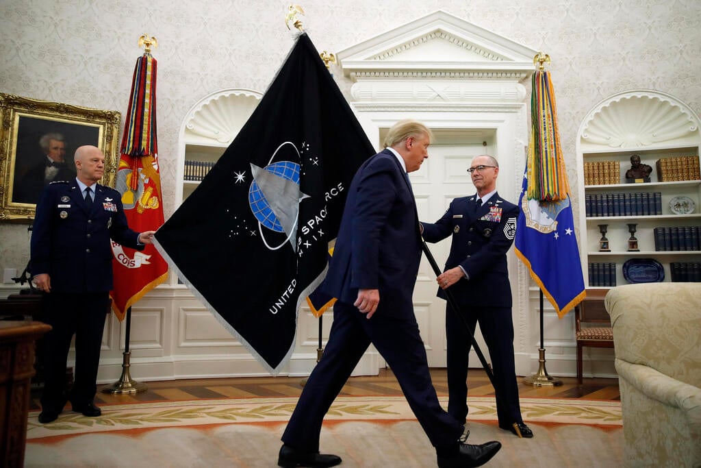 Chief of Space Operations at United States Space Force Gen. John Raymond, left, and Chief Master Sgt. Roger Towberman, right, hold the U.S. Space Force flagֲ as President Donald Trump walks past it, in the Oval Office of the White House in Washington 